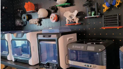 A 3D printing studio with a row of 3D printers on the table and many 3D printed works hanging on the walls.